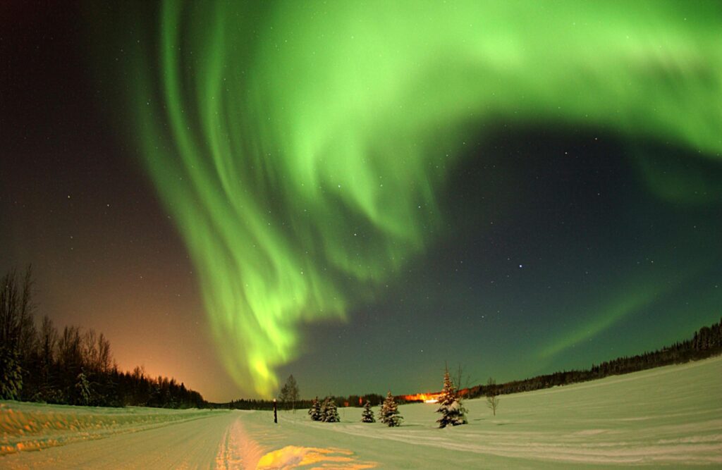 Vibrant green aurora borealis lighting up the snowy winter night sky in a remote wilderness.
